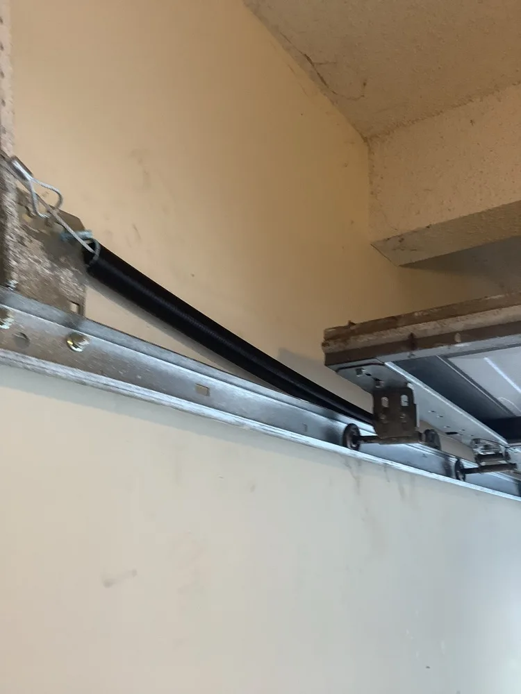 Extension spring stretched taut alongside the horizontal track above a raised garage door, with a roller and hinge riding in the track beneath it