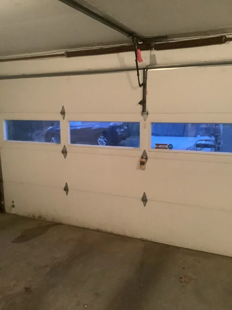 Long white double garage door closed from inside, a row of three windows showing parked vehicles outside and the opener arm running down to the top section