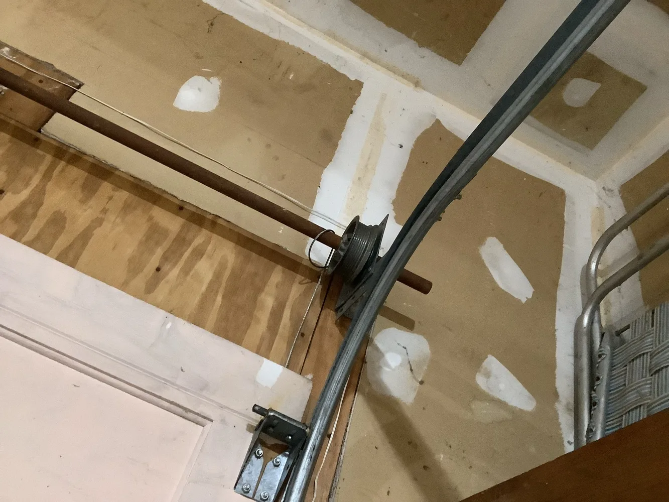 Cable drum on the end of a torsion shaft at the point where the vertical track curves into the horizontal, with the lift cable wound onto the grooved drum