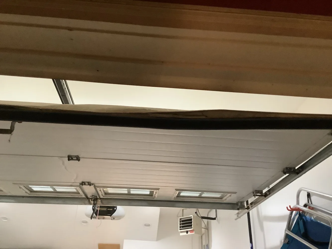 Underside of a sectional garage door parked on its overhead tracks, glazed lights along its end section, with a garage door opener and a wall-mounted heater below